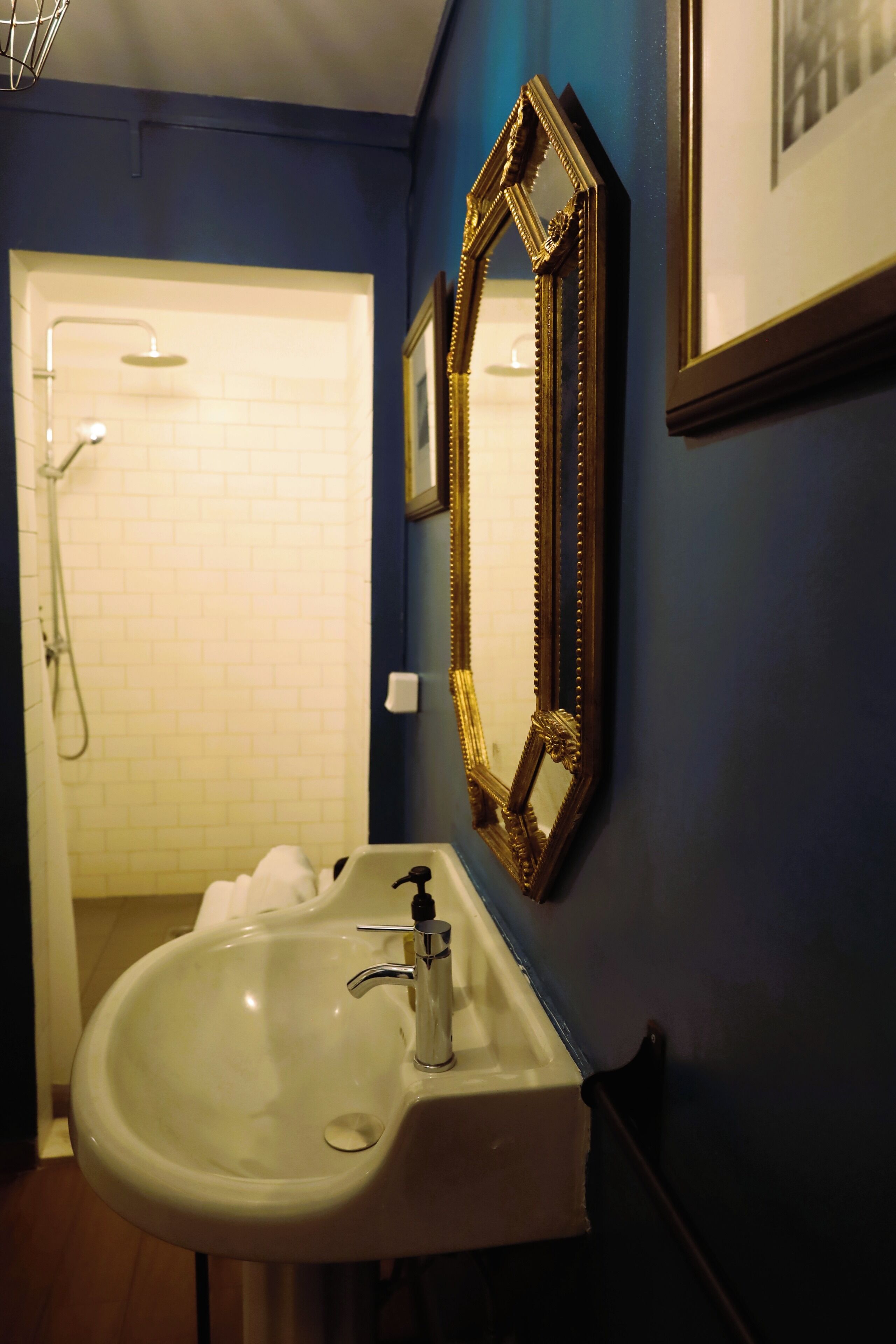 Une salle de bain avec un lavabo blanc, un miroir encadré d’or et un espace douche.