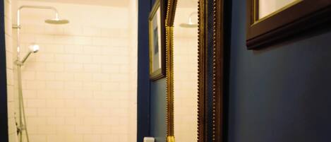 Une salle de bain avec un lavabo blanc, un miroir encadré d’or et un espace douche.