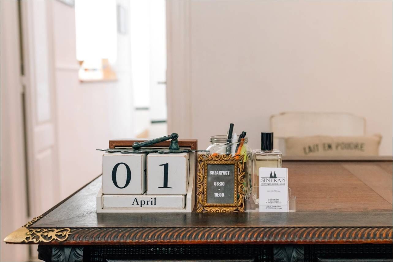A wooden table with a calendar marked '01 April', a framed picture with a clock, a jar with a spoon, and a bottle with a label.