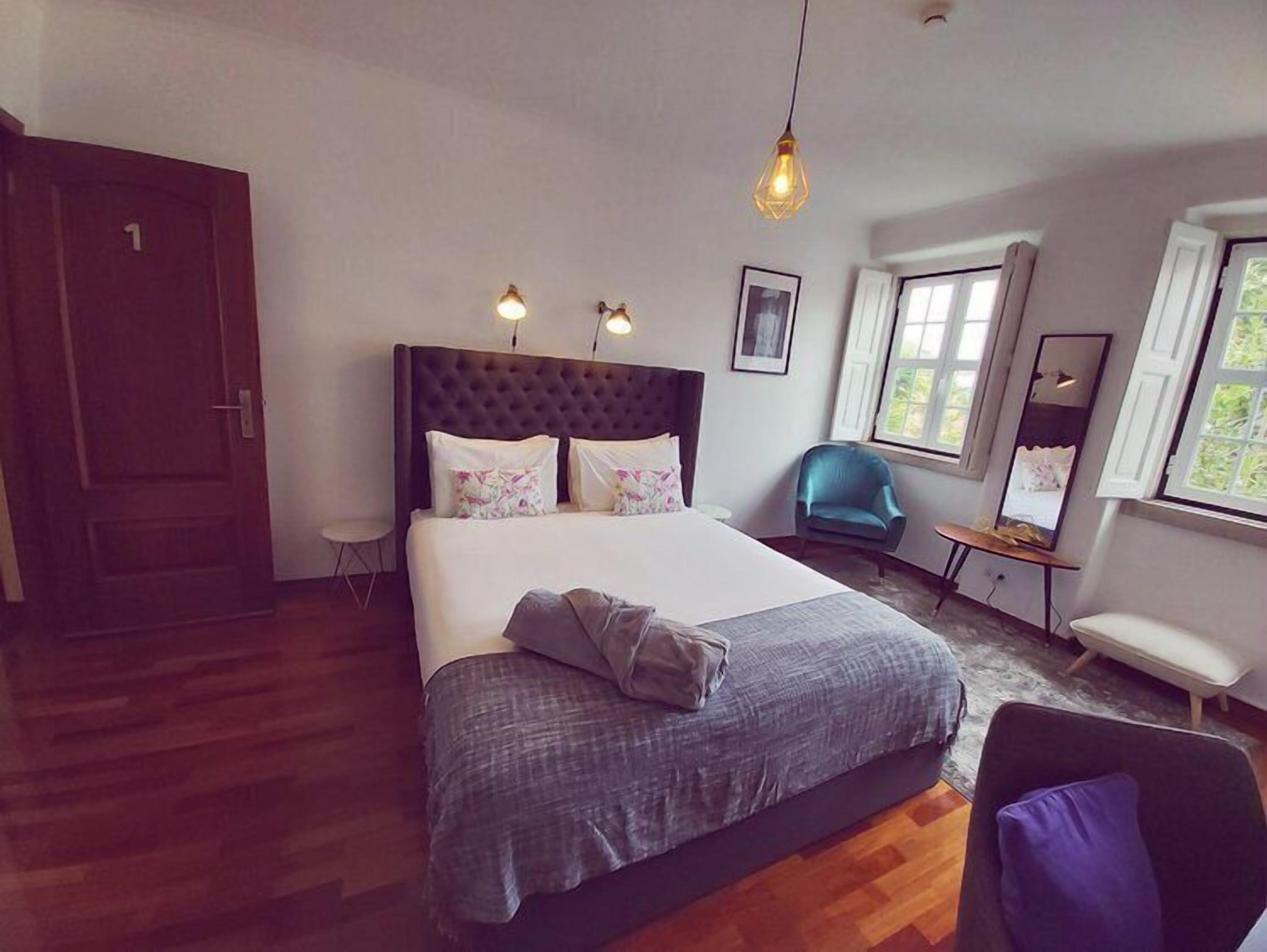 A bedroom with a large bed, a chair, a desk, and a mirror.