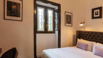 A bedroom with a large bed, a wooden door, and framed pictures on the walls.