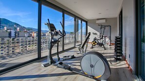 A modern gym with large windows, exercise equipment, and a view of the cityscape. - Chic, Spacious Condo | Great Walkability, Pool, Gym, Rooftop Views (Puerto Vallarta)