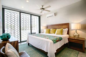 A hotel room with a bed, a desk, a chair, a ceiling fan, and a window with a view.