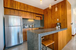 A modern kitchen with wooden cabinetry, a stainless steel refrigerator, a granite countertop, and pendant lighting.