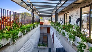 A narrow, covered outdoor corridor with a glass roof, flanked by planters with greenery and a mural on the right wall. - Chic, Spacious Condo | Great Walkability, Pool, Gym, Rooftop Views (Puerto Vallarta)