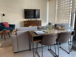 A modern living room with a sofa, a coffee table, a dining table with chairs, a television, and a decorative cabinet.
