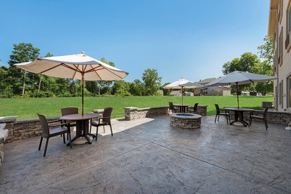 Un espace extérieur aménagé en terrasse, avec un sol en pierre, plusieurs tables et chaises, et de grands parasols.