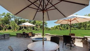 Une terrasse extérieure avec une table ronde, des chaises et deux grands parasols.