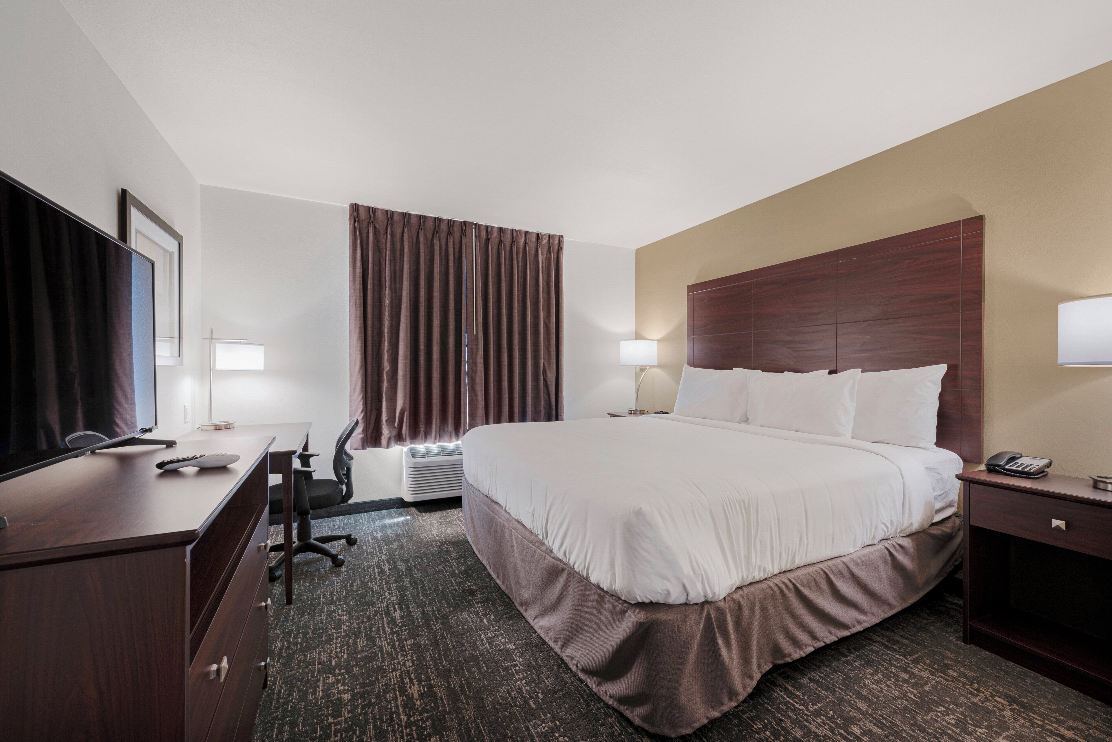 A hotel room with a large bed, a desk with a computer, a chair, a TV, and a lamp.