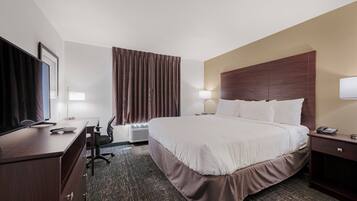 A hotel room with a large bed, a desk with a computer, a chair, a TV, and a lamp.