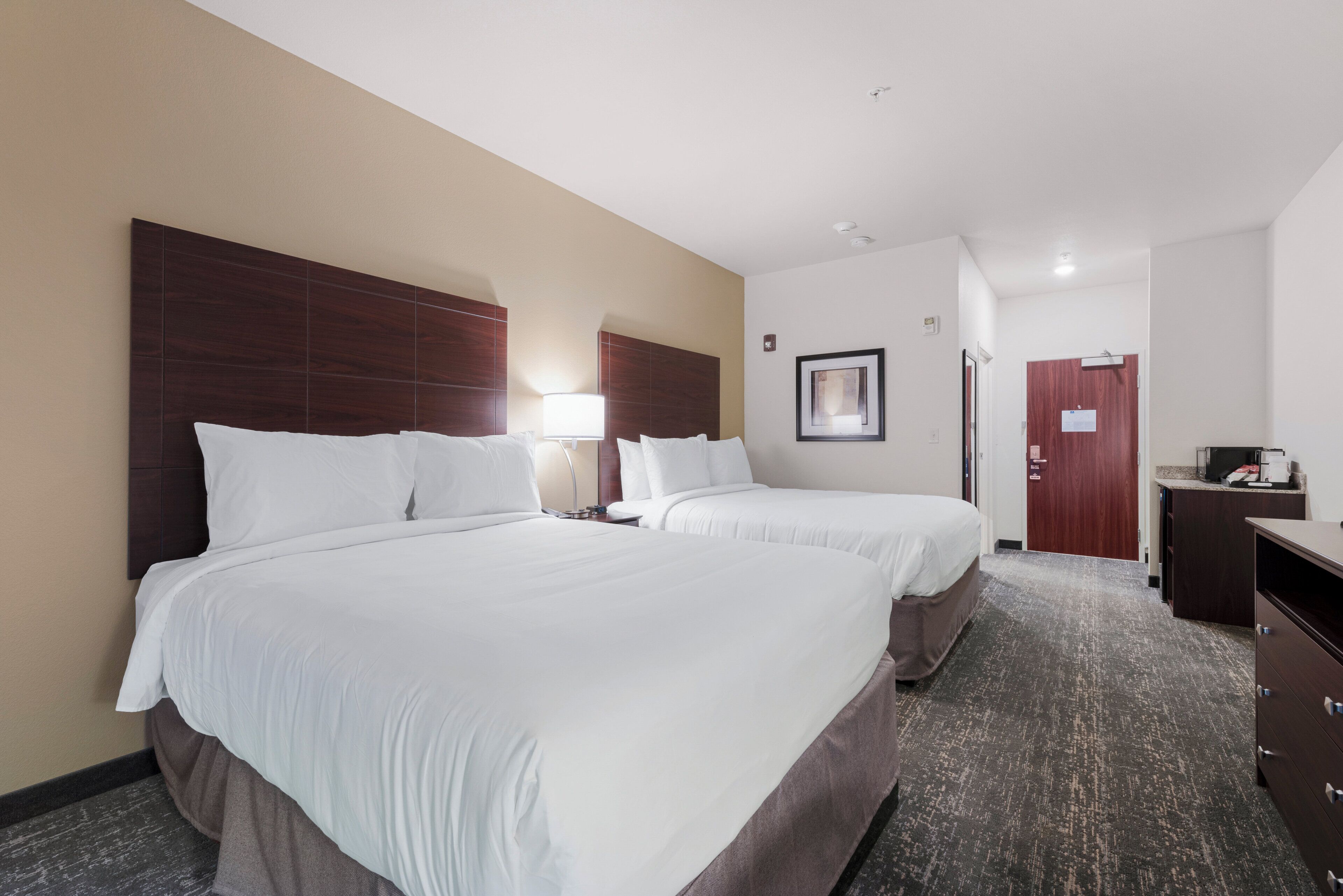 A hotel room with two beds, a desk, a chair, and a wardrobe.
