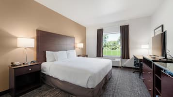 A hotel room with a large bed, two bedside tables with lamps, a desk with a chair, a TV, and a window with curtains.