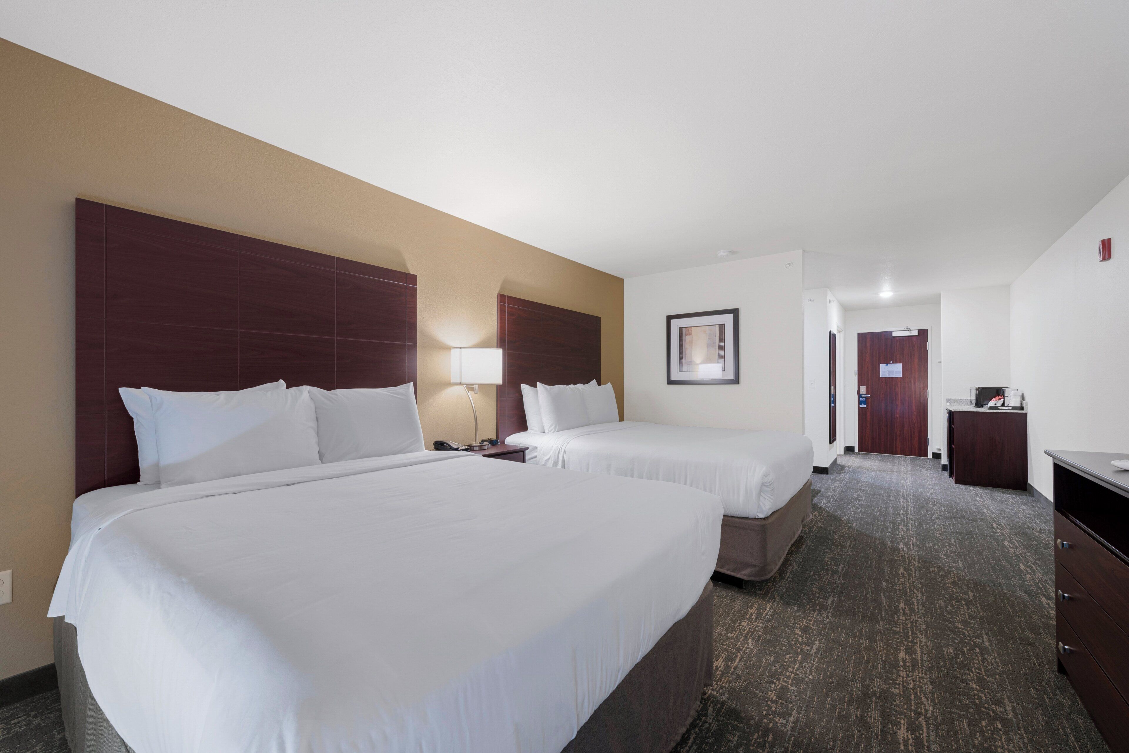 A hotel room with two beds, a desk, a lamp, and a framed picture on the wall.
