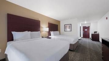A hotel room with two beds, a desk, a lamp, and a framed picture on the wall.