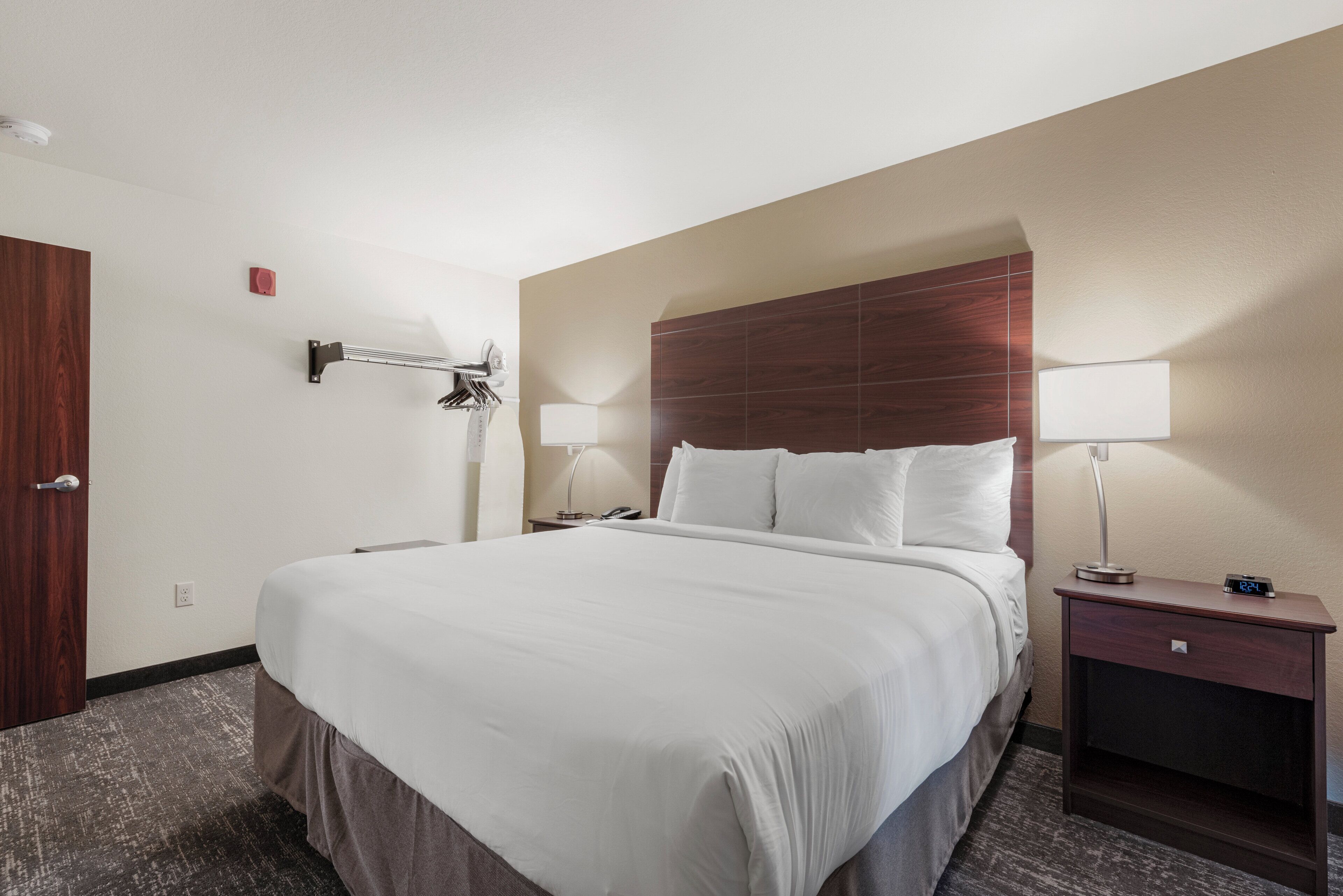 A hotel room with a large bed, two bedside tables, a nightstand, a wooden door, and a wall-mounted lamp.