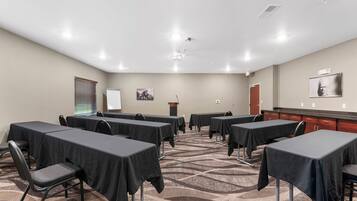 Un salón de conferencias con mesas, sillas, un atril y una pantalla para proyector.