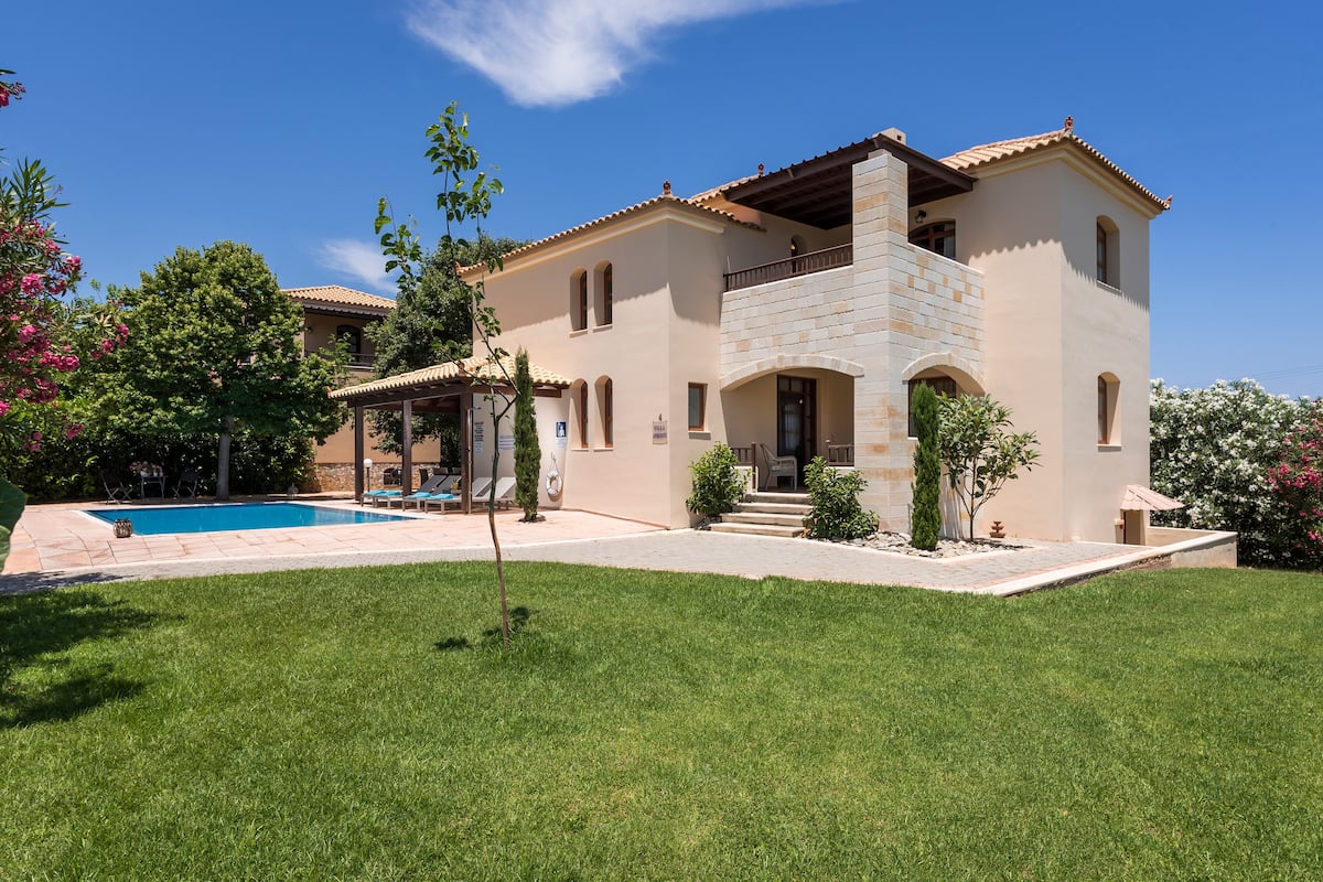 A two-story house with a swimming pool, a covered patio, and a well-maintained lawn.