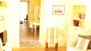 Una sala de estar con sofá, sillón y televisor. Se observa un comedor al fondo.