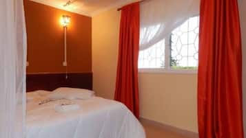 A bedroom with a bed, a nightstand, a wall-mounted lamp, and a window with curtains.