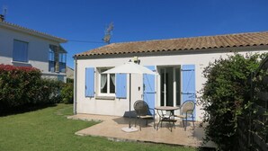 A small house with a patio, a white umbrella, and a table with two chairs. - Lavender Cottage is a one bedroom gîte with private terrace and garden (Étaules, Nouvelle-Aquitaine,)