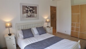 Un dormitorio con cama, dos mesitas de noche, una lámpara, un cuadro y una zona de ducha.