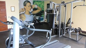 Une salle de sport équipée de matériel d’exercice, d’un tapis de course et d’un mur orné d’une affiche sur le thème du fitness.