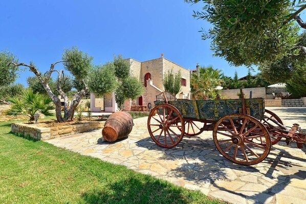 A stone building with a red door and a cart with large wheels. - Grecian Villas Chania (Platanias)