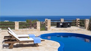Ein Pool mit Liegestühlen und einer Steindeck, mit Blick auf ein Gewässer.