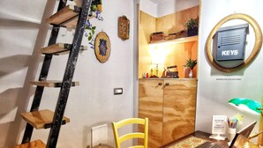 A compact room with a wooden desk, a laptop, a chair, a ladder, a wall-mounted light, and a small cabinet with keys. - Miracolo Al Duomo (Naples)