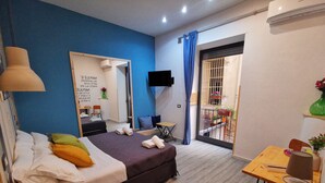 A modern bedroom with a bed, a desk, a chair, a sewing machine, and a balcony with potted plants. - Miracolo Al Duomo (Naples)