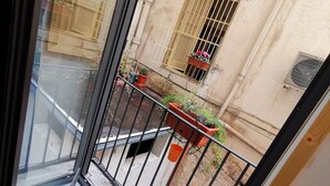A balcony with a metal railing, potted plants, and a view of a building with a window and a door. - Miracolo Al Duomo (Naples)