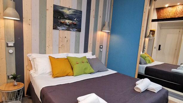 A hotel room with a large bed, a small bedside table with a lamp, a mirror, and a painting on the wall. - Miracolo Al Duomo (Naples)