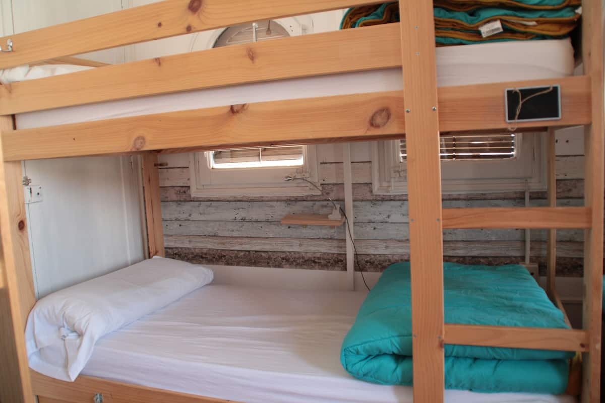 A bunk bed room with a window, wooden walls, and a small shelf.