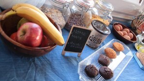 Un desayuno con un tazón de frutas, frascos de granola y chispas de chocolate, un letrero que dice “Hecho en Casa” y una bandeja de galletas.