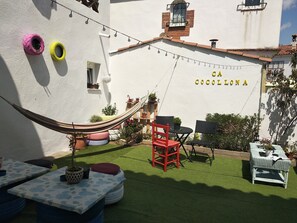 Un patio con una hamaca, mobiliario exterior y una pared con el nombre "CA COCOLLONA".