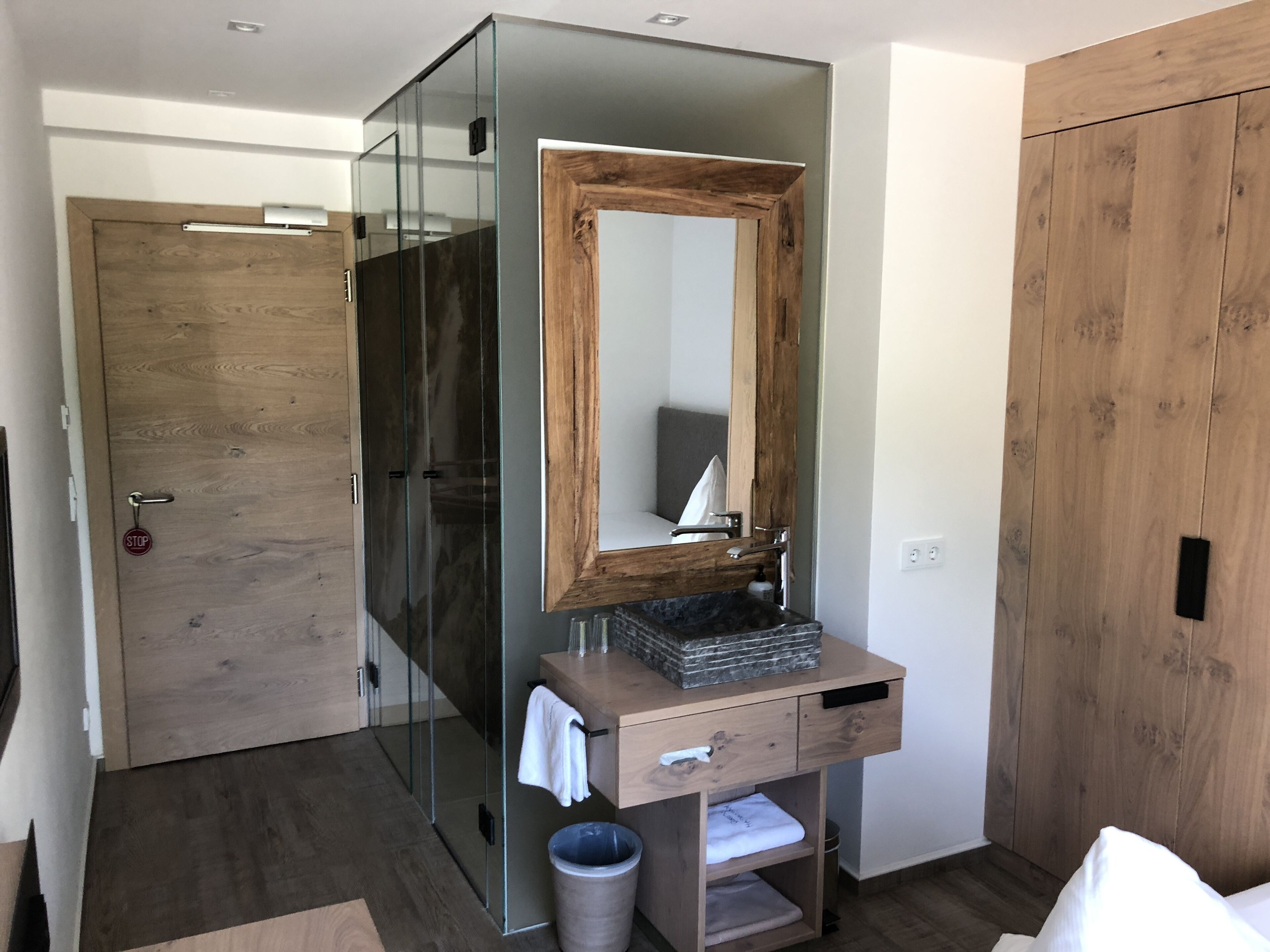 A modern bathroom with a glass shower enclosure, a wooden vanity with a mirror, and a wooden wardrobe.