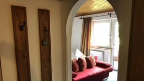 Una habitación con un sofá rojo, una puerta de madera con un cartel de 'STOP' y una ventana con cortinas.