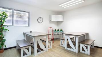 Una habitación moderna y luminosa con piso de madera, una mesa de comedor con bancos, una silla roja, un reloj, una ventana con persianas y una planta en maceta.