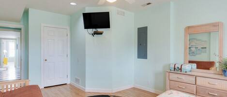A bedroom with a bed, a dresser, a television mounted on the wall, and a ceiling fan.