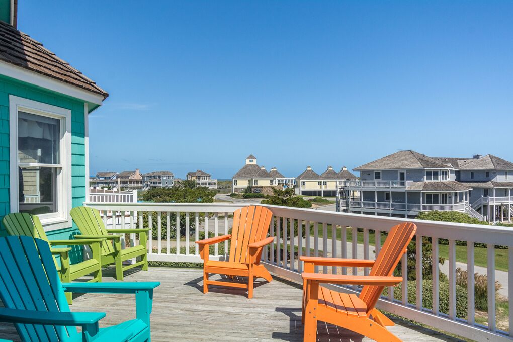 A wooden deck with colorful Adirondack chairs overlooking a coastal community with houses.