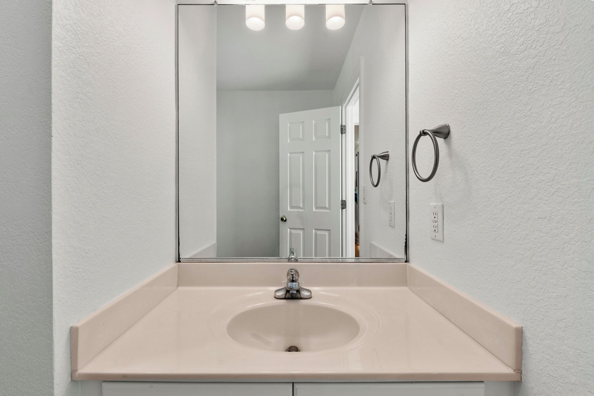 Un baño con un lavamanos color beige, un espejo grande y una puerta blanca al fondo.