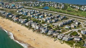 An aerial view of a coastal residential area with houses, roads, and a beach.