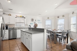 A modern kitchen with white cabinets, a stainless steel refrigerator, and a dining area with a table and chairs.