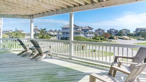 A covered wooden deck with lounge chairs and a white railing, overlooking a residential area with houses and greenery.