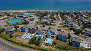 An aerial view of a coastal residential area with houses, a beach, and a swimming pool complex.