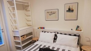 A bedroom with a bed, a white wardrobe, two framed pictures, and a small table with a lamp. - Rondone Bianco 5-7 (Como)
