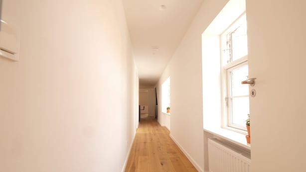 Un couloir étroit avec un plancher en bois et des murs blancs.