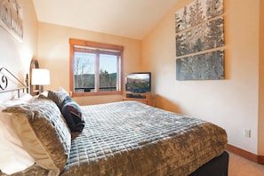 Un dormitorio con cama, televisión, ventana y obras de arte en la pared.