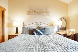 Ein Bett mit gesteppter Bettdecke, zwei Nachttischlampen, ein Nachttisch aus Holz, ein Spiegel und ein Holzstuhl.