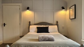 Ein ordentlich bezogenes Bett mit einem gemusterten Überwurf, zwei Nachttischlampen und einem gerahmten Bild an der Wand.